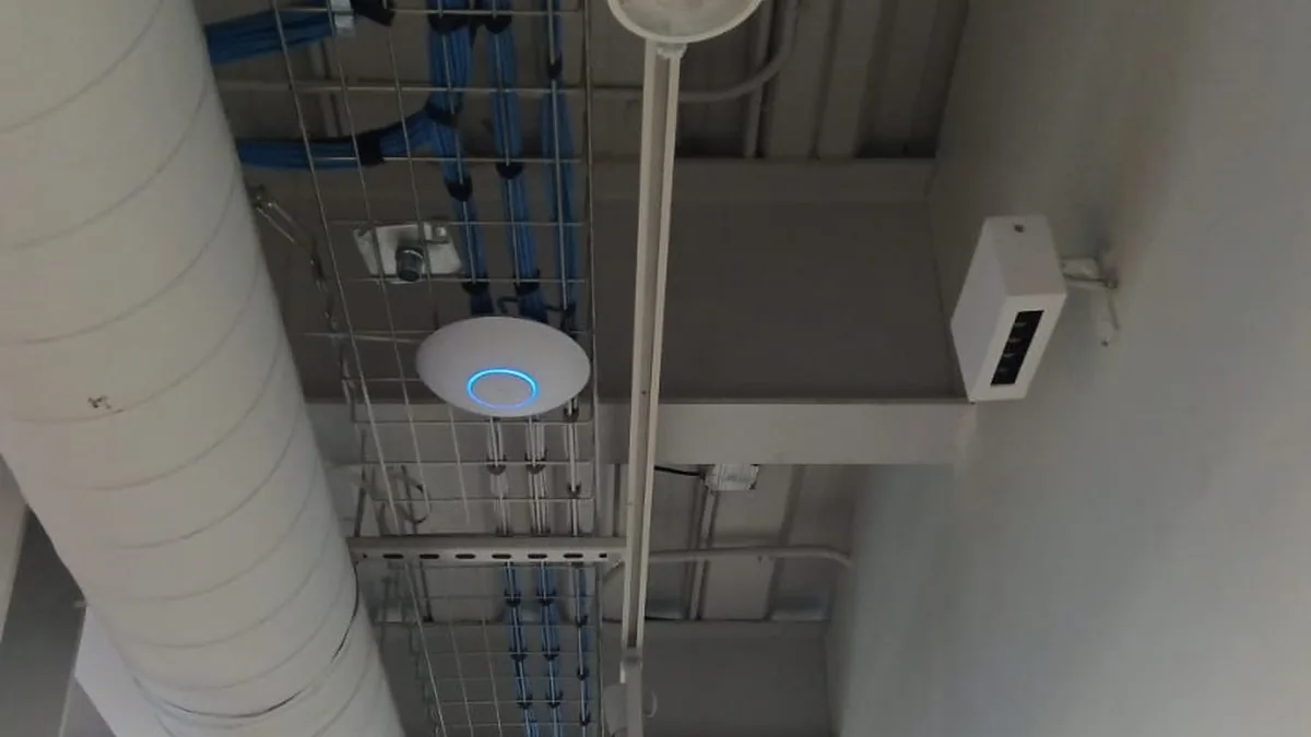 Punto de acceso y cableado de red sobre la escalerilla del techo, junto al ducto de aire de una nave